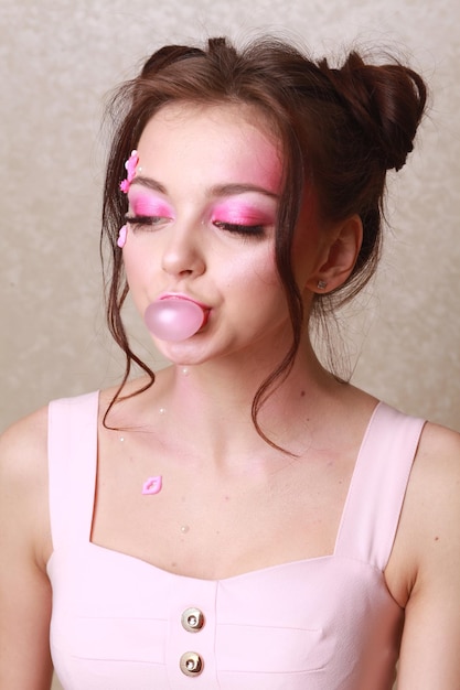 Foto giovane donna con il trucco rosa che mastica gomma da masticare contro il muro