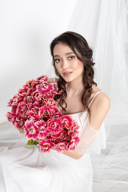 Giovane donna con tulipani rosa in abito bianco mani