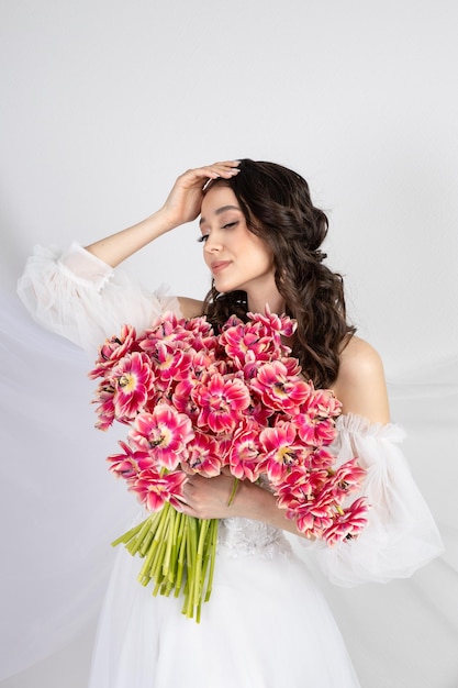 Молодая женщина с розовыми тюльпанами в руках белое платье