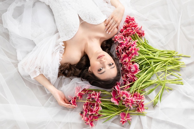 Giovane donna con tulipani rosa in abito bianco mani