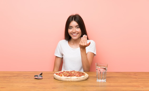 Young woman with a pizza inviting to come with hand. Happy that you came