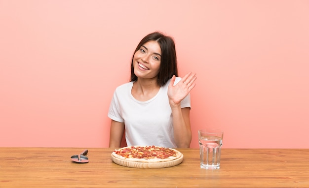 Young woman with a pizza saluting with hand with happy expression