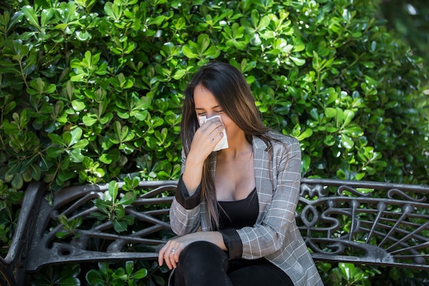 茂みの近くで鼻を吹く花粉症の若い女性