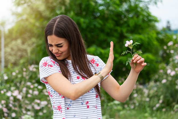 Young woman with Pollen allergy holding a flower and saying no..