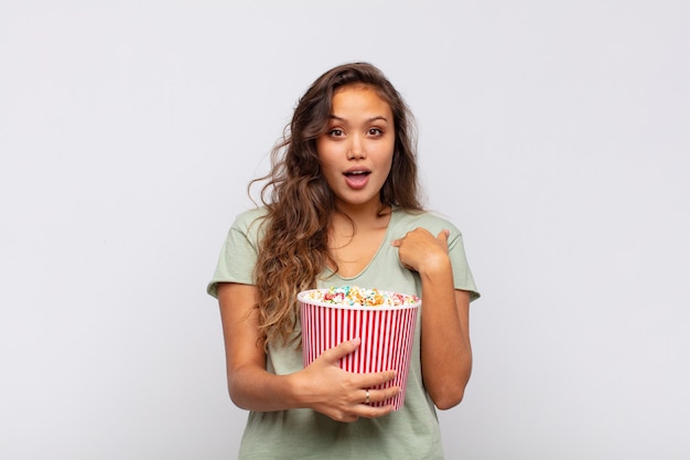 Young woman with a pop conrs bucket feeling happy, surprised and proud, pointing to self with an excited, amazed look