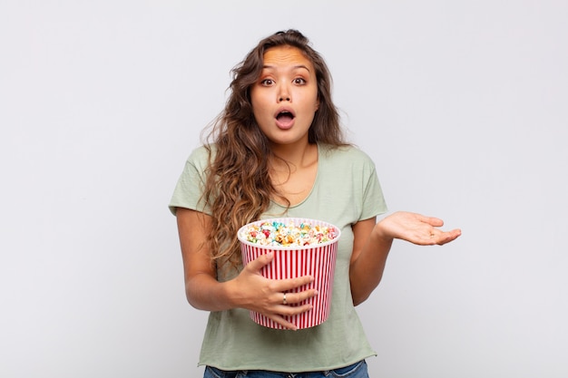 Young woman with a pop conrs bucket open-mouthed and amazed, shocked and astonished with an unbelievable surprise