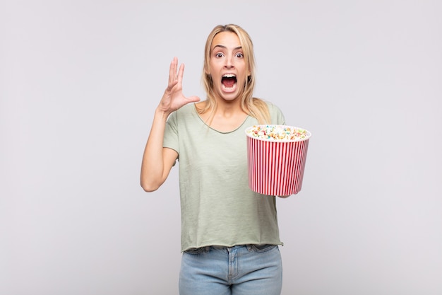 Young woman with a pop corns bucket screaming with hands up in the air, feeling furious, frustrated, stressed and upset