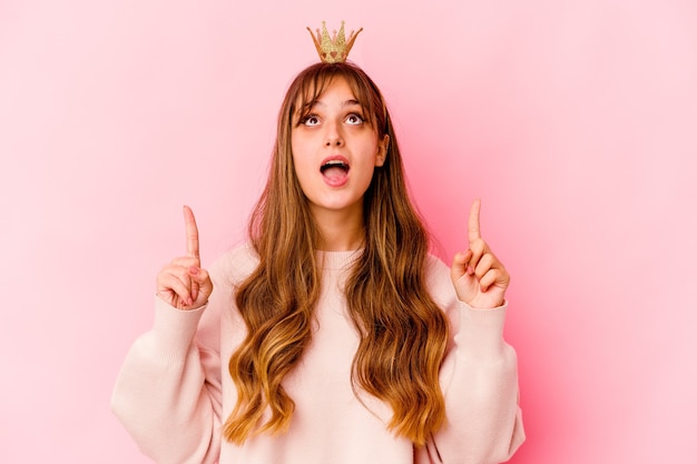 Young woman with princess crown isolated pointing upside with opened mouth