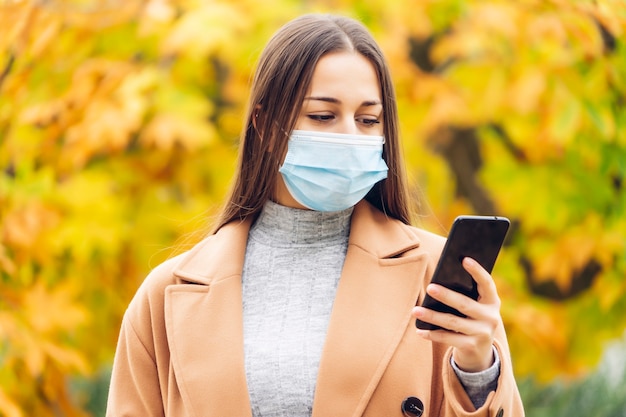 Young woman with a protective mask in the autumn park