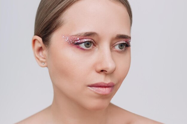 Young woman with purple and pink eye shadow and glitter on the eyelids on a gray background