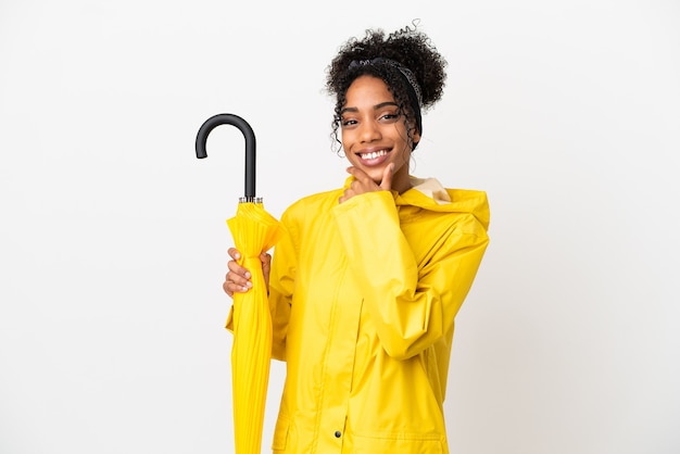 Young woman with rainproof coat and umbrella isolated on white background happy and smiling