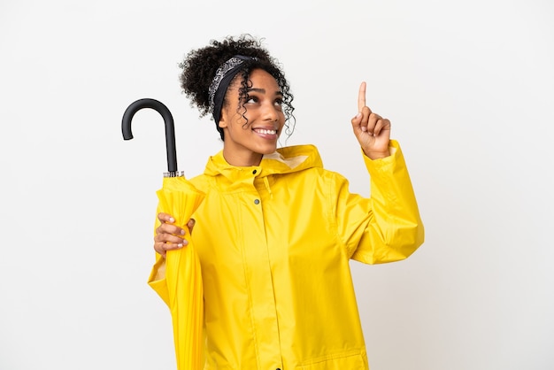 좋은 아이디어를 가리키는 흰색 배경에 격리된 방수 코트와 우산을 가진 젊은 여성
