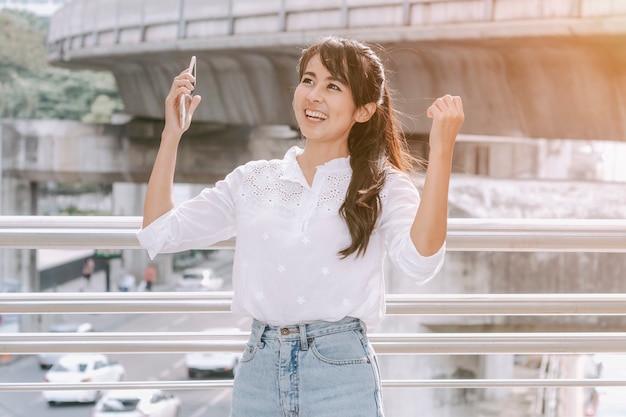 Young woman with raised hands shouting and cheering at city outdoor.