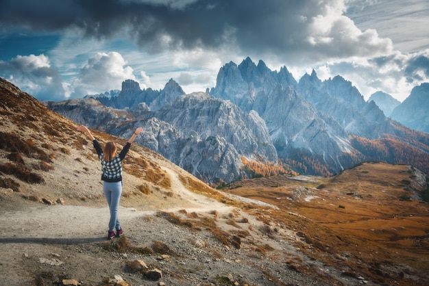 Young woman with raised up arms and majestic mountains at sunset in autumn