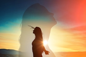 Young woman with raising hands on the sunset sky background.