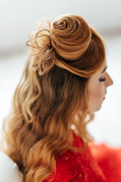 Young woman with red hair in a bright red dress in a light room near a white wall