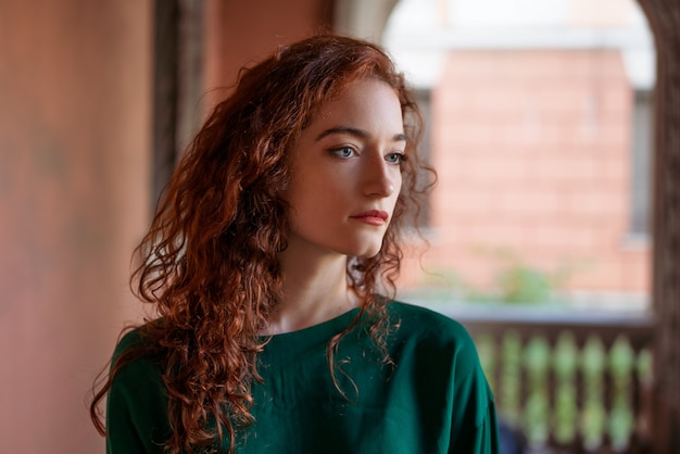 young woman with red hair and freckles, on the street near the building