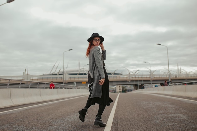 Young woman with red hair posing in a hat on the street