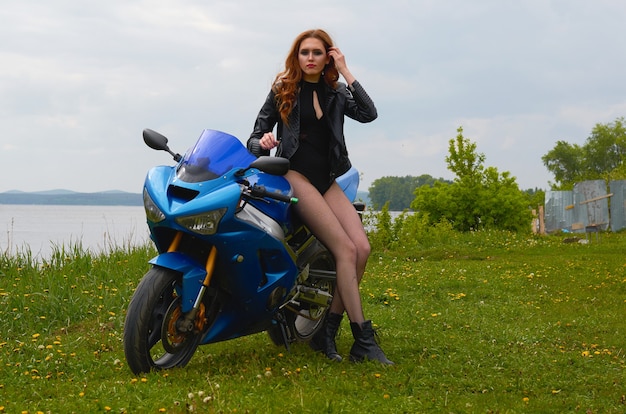 A young woman with red hair and wearing a black leather jacket on a blue sports motorcycle