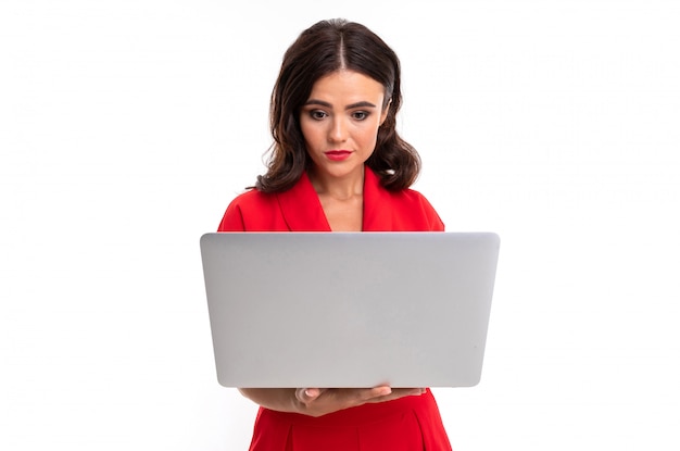 Photo a young woman with red lips, bright makeup, dark wavy long hair, in a red suit, stands with a white laptop