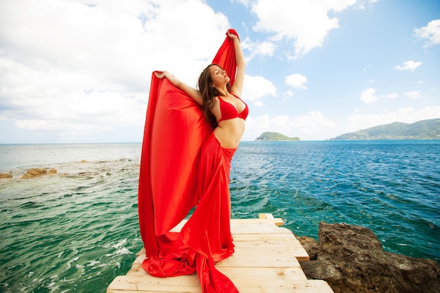 Young woman with red skirt and  fabric like a wings. Vogue style.