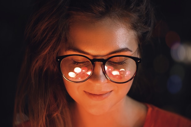 young woman with reflection of glowing light balls in her eye glasses
