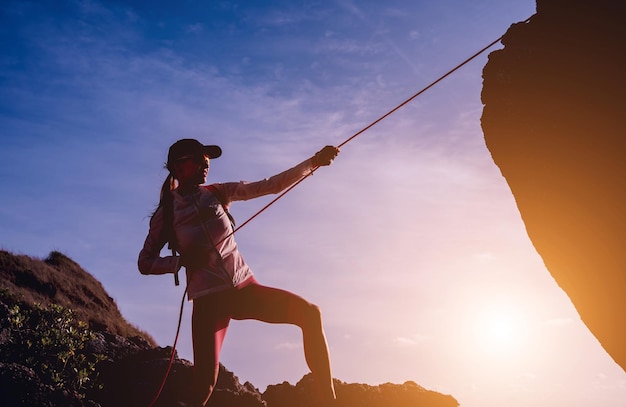 Young woman with a rope climbs to the top in the mountains near the ocean