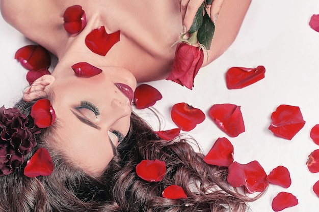 Young woman with rose lying among rose petals