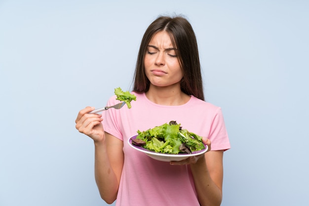 Young woman with salad over isolated blue wall