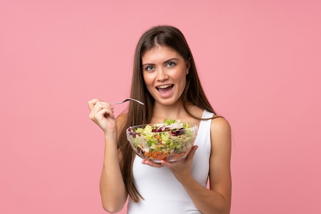 Giovane donna con insalata sopra la parete rosa isolata