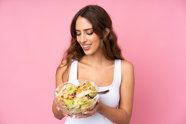 Young woman with salad over isolated pink wall