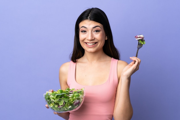 Молодая женщина с салатом над изолированной фиолетовой стеной