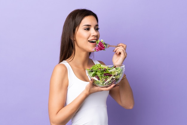 Giovane donna con insalata isolata sulla parete viola