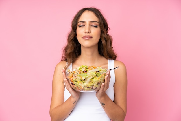 Young woman with salad over pink wall