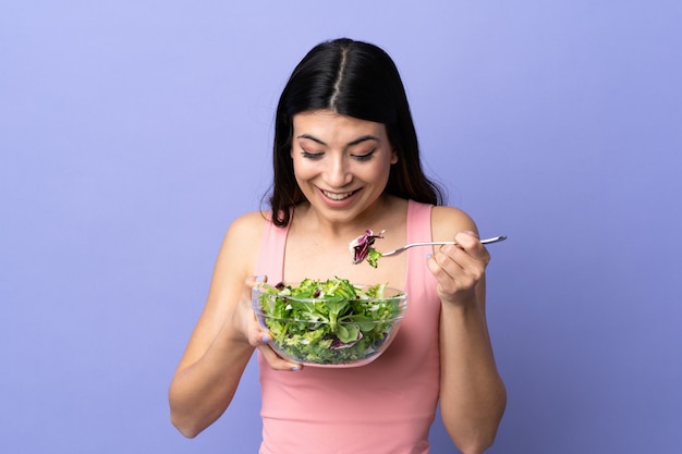 Young woman with salad over purple wall