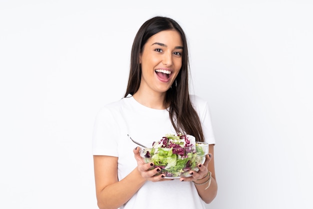 Young woman with salad on white wall