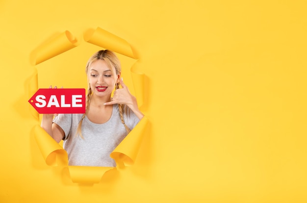 Photo young woman with sale inscription sign on torn yellow paper surface