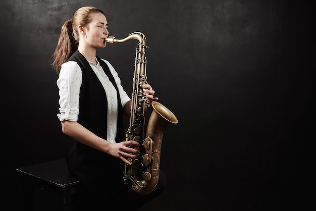 Young woman with saxophone on black background