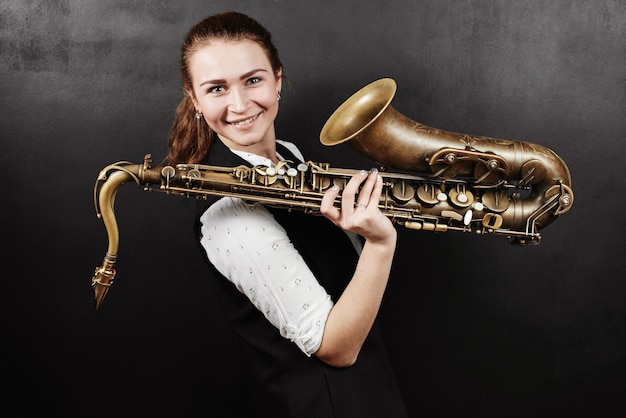 Young woman with saxophone on black background