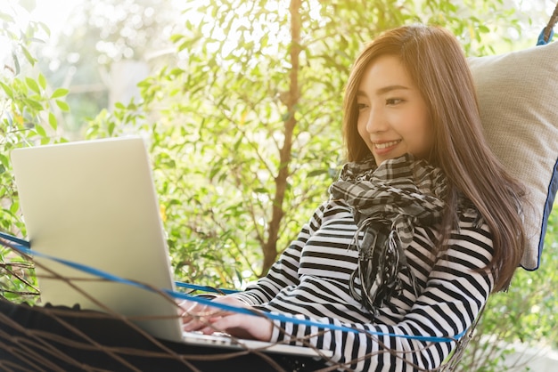 La giovane donna con il computer portatile di uso della sciarpa che si trova in amaca, stile di vita indipendente concettuale, lavora ovunque