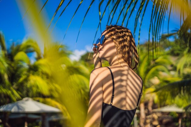 Young woman with the shadow of the palm leaf on her back relaxing on the seaside