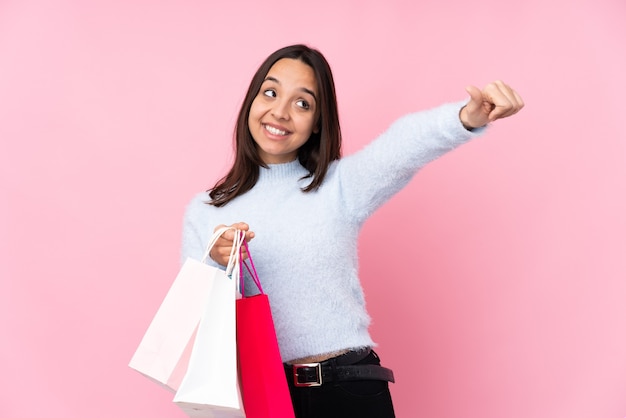 제스처를 엄지 손가락을주는 고립 된 분홍색 벽 위에 쇼핑백을 가진 젊은 여자