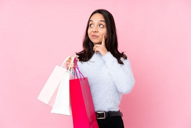 Young woman with shopping bag over isolated pink wall thinking an idea while looking up