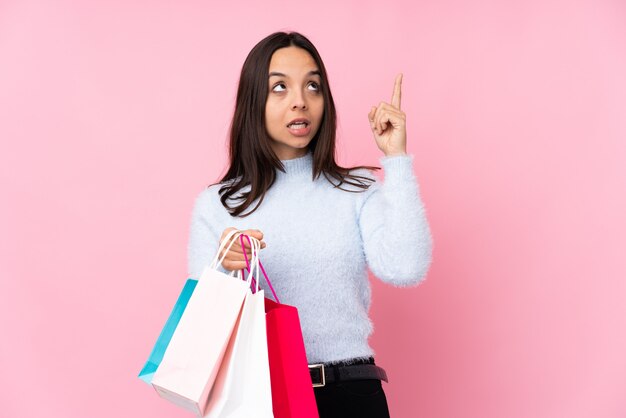 Young woman with shopping bag over pink wall intending to realizes the solution while lifting a finger up