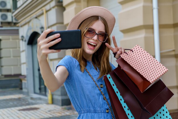 夏の日に街を歩いてselfieを作る買い物袋を持つ若い女