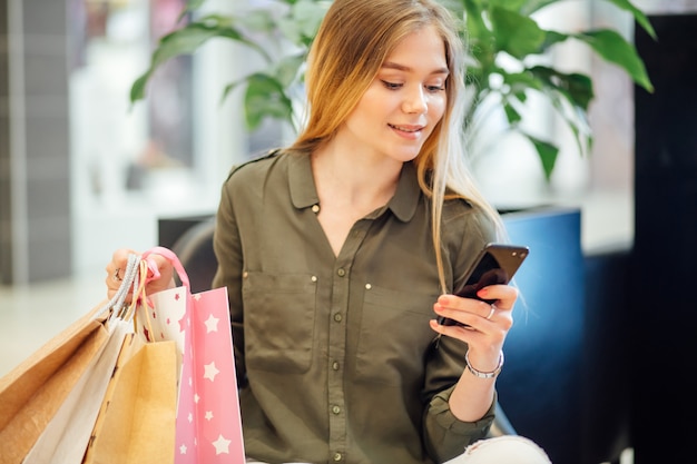 Foto giovane donna con i sacchetti della spesa facendo uso del suo smart phone per acquistare