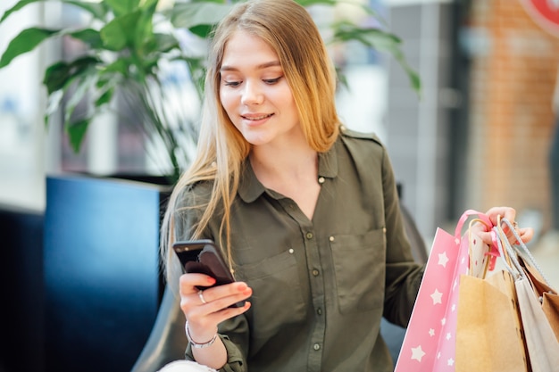 買い物に彼女のスマートフォンを使用して買い物袋を持つ若い女性