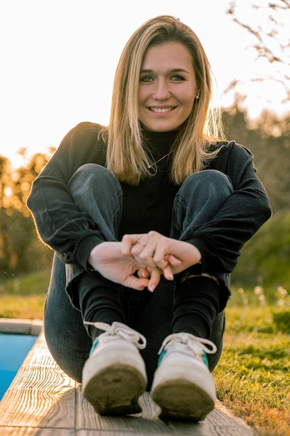 Young woman with short blonde hair sitting on the floor in casual clothes and smiling at the camera