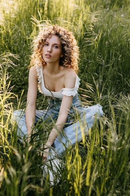 背の高い緑の草のフィールドに座っている短い巻き毛の若い女性