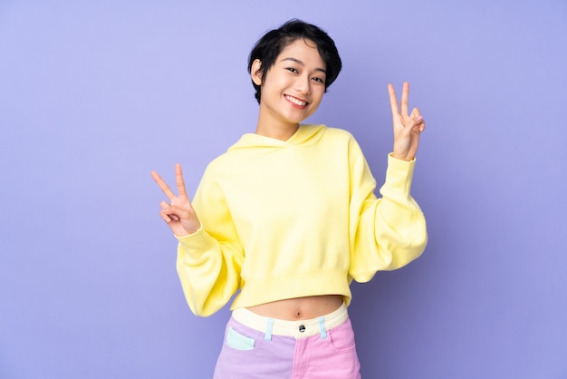 Young woman with short hair over isolated purple showing victory sign with both hands